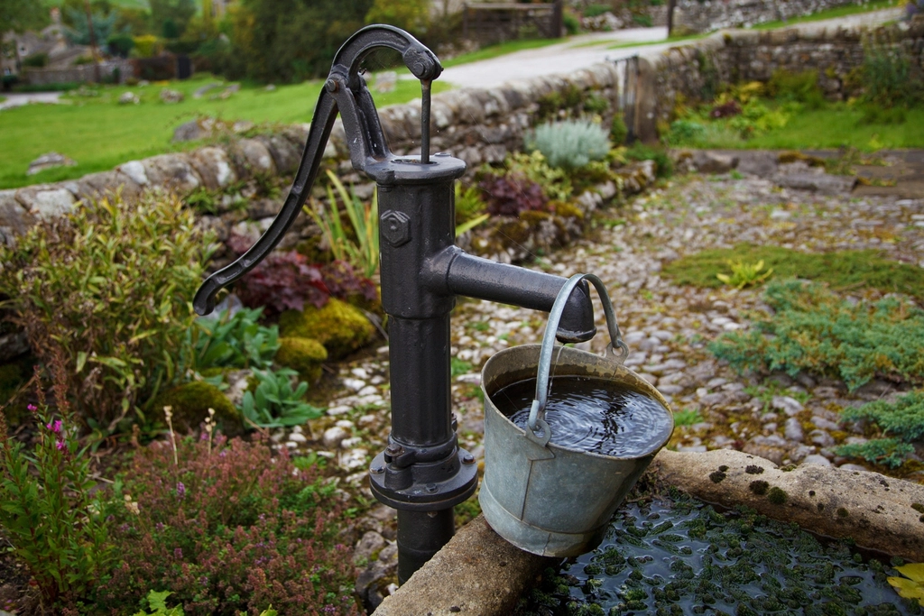 A metal bucket sitting on a well in a garden