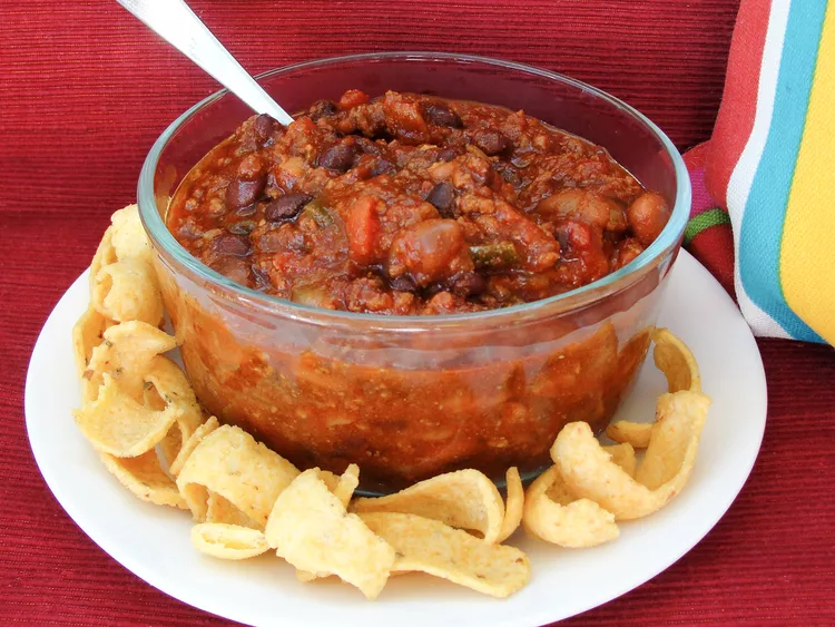 A bowl of chilli sitting on a plate with cornbread