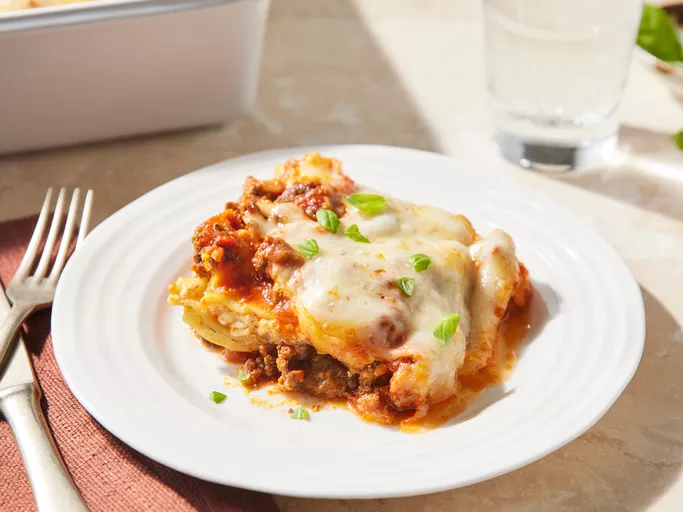 A slice of Lasagna sitting on a white bowl with a fork
